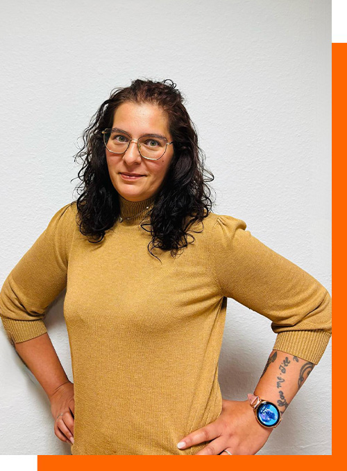 Person mit Brille und schwarzem Haar lächelt leicht; trägt gemustertes Kleid und hat Stern-Tattoos.