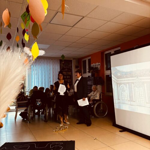 Zwei elegant gekleidete Personen sprechen vor Publikum neben einer Leinwand mit Bild