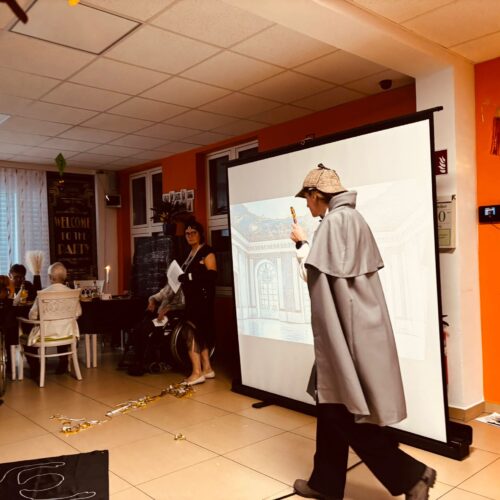 Ein Mann in Sherlock Holmes Kostüm läuft mit ernster Miene vor einer Leinwand entlang