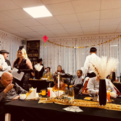 Mehrere elegant gekleidete Erwachsene feiern an reich dekorierten, goldglänzenden Tischen