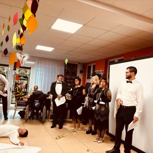 Eine Gruppe elegant gekleideter Menschen steht in einem bunt dekorierten Raum zusammen