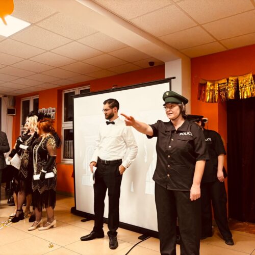 Eine Frau in Polizeiuniform gestikuliert freundlich, dahinter Menschen in festlicher Kleidung