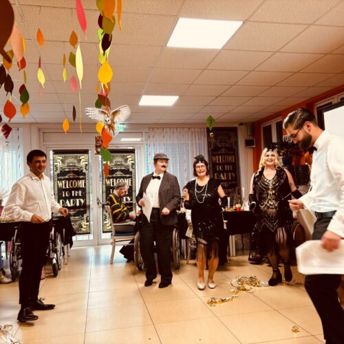 Fünf elegant gekleidete Erwachsene lachen in einem festlich dekorierten Raum