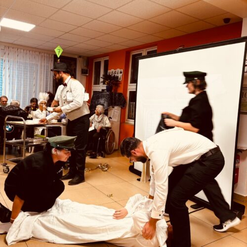 Vier Erwachsene in Uniform führen ein Theaterstück mit einer am Boden liegenden Person auf