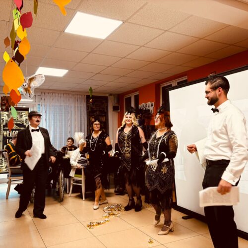 Fuenf elegant gekleidete Erwachsene mit festlichem Gesichtsausdruck bei einer Feier in bunt dekoriertem Raum