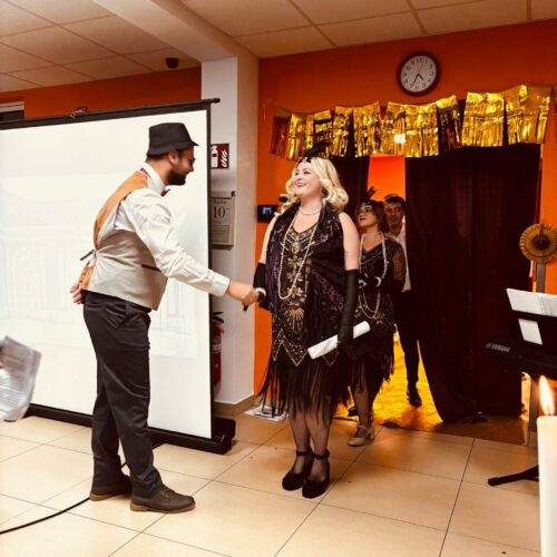 Ein Mann mit Hut und Weste begrüßt freundlich eine Frau im schwarzen Charleston Kleid