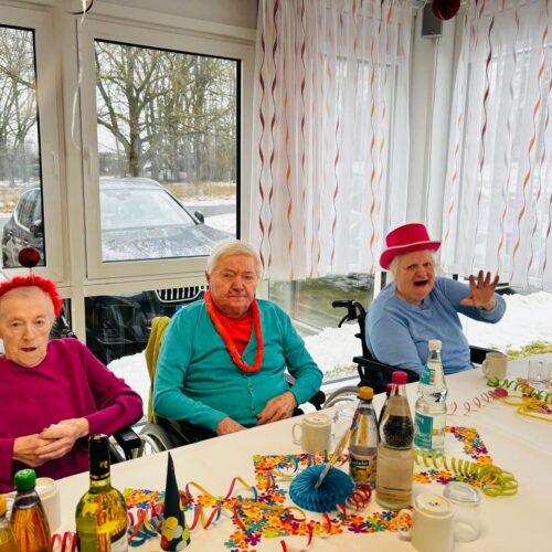 Drei ältere Menschen in bunten Outfits feiern fröhlich in einem bunt geschmückten Raum