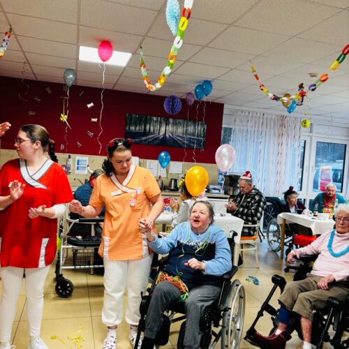 Mehrere Senioren und Pfleger feiern fröhlich geschmückt mit Luftballons und Girlanden