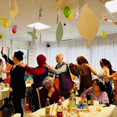Eine fröhliche Gruppe älterer Menschen tanzt verkleidet als Polonaise durch einen bunt geschmückten Raum