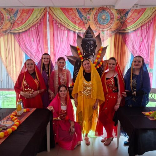 Eine Gruppe bunt gekleideter Frauen mit fröhlichen Gesichtern vor einem großen Buddha