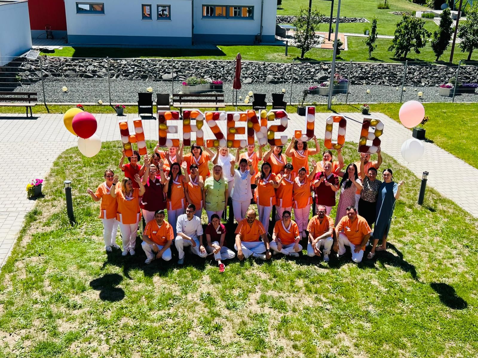 Laechelnde Gruppe in orange und weiss haelt Danke Schilder und Ballons