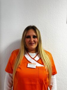 Valentina Franz mit langen blonden Haaren laechelt in oranger Pflegekleidung